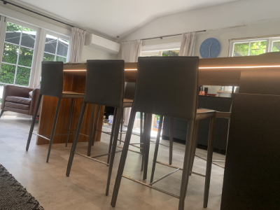 Modern underbench LED lighting installed under a wooden kitchen bench, highlighting the workspace with the house interior in the background.