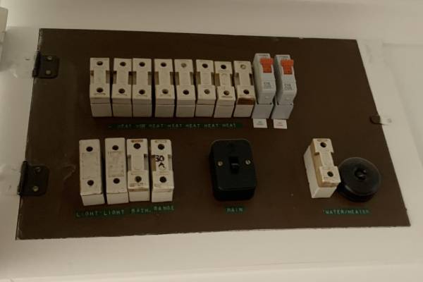 Old fuseboard with ceramic fuses and outdated wiring, showing a need for electrical upgrade.